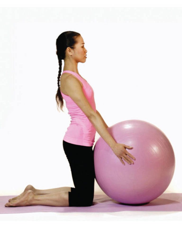 mulher oriental de perfil com trança nos cabelos, veste calça preta e blusa rosa, ajoelhada segura uma bola de Pilates rosa