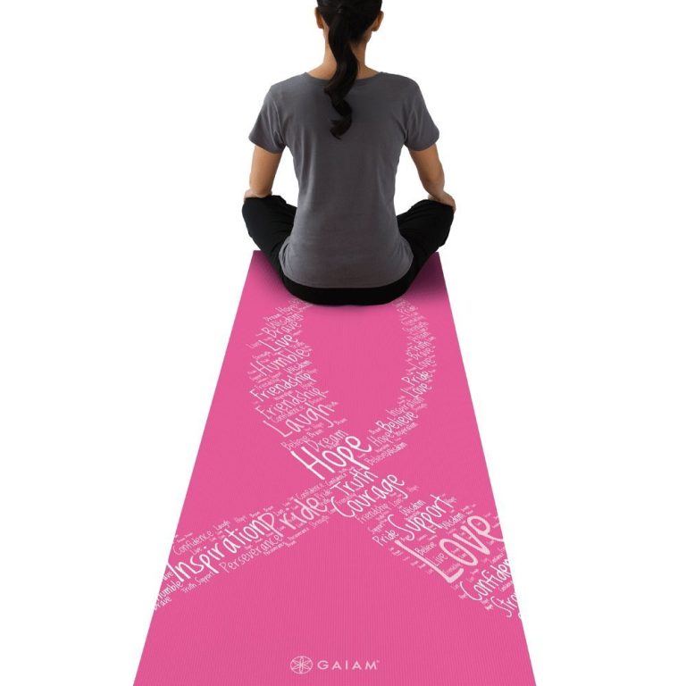 mulher sentada de costas com blusa cinza e calça preta em cima de mat de yoga rosa com o símbolo da fita de causa branco desenhado