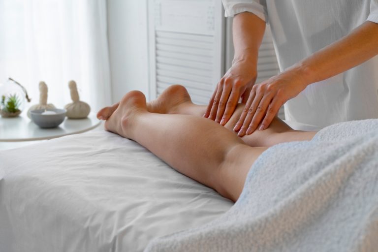 Mulher recebendo massagem de drenagem linfática nas pernas em uma maca, com foco nos movimentos suaves.